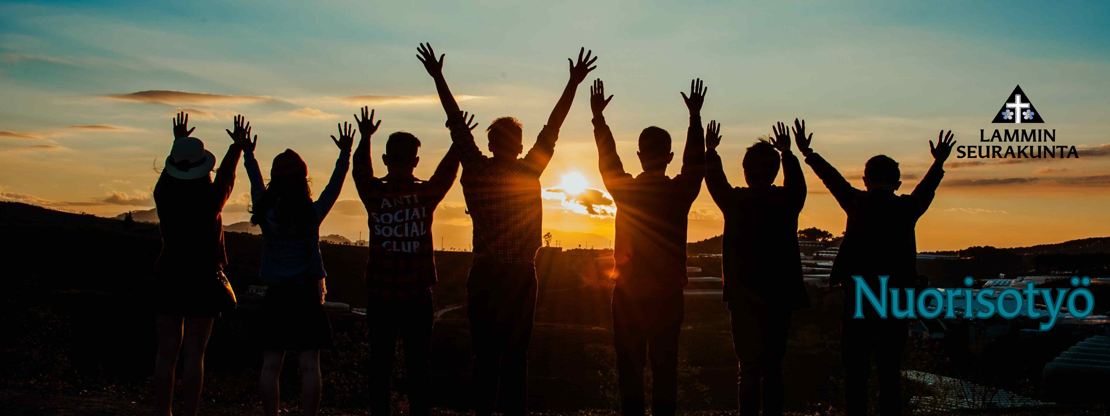 7 nuorta ihmisistä seisoo selin katsoen auringon laskua kädet ylhäällä.